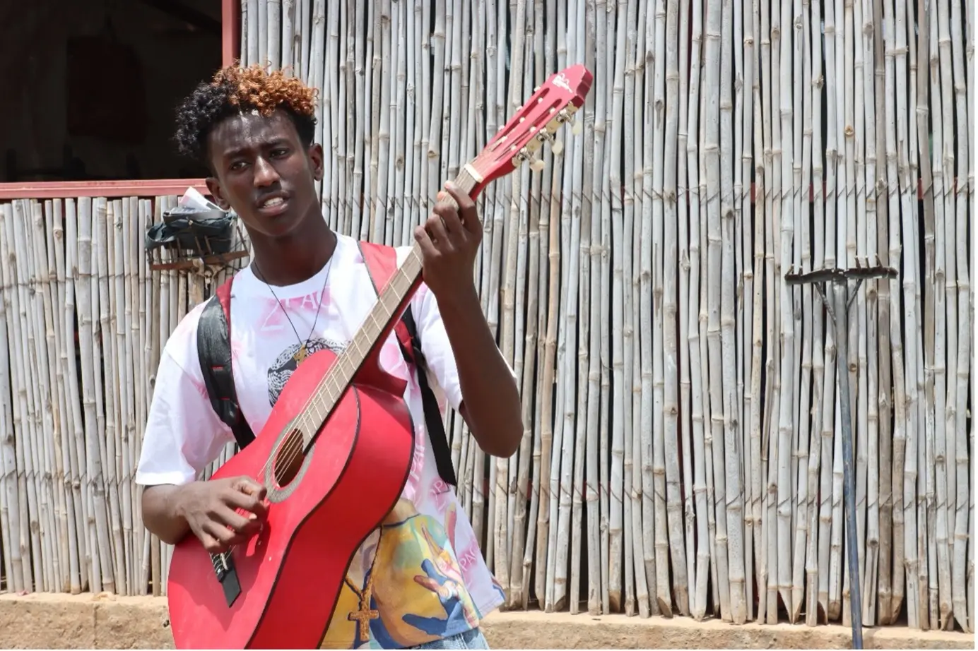 Yared playing guitar outside a school in Umrakoba camp, Sudan